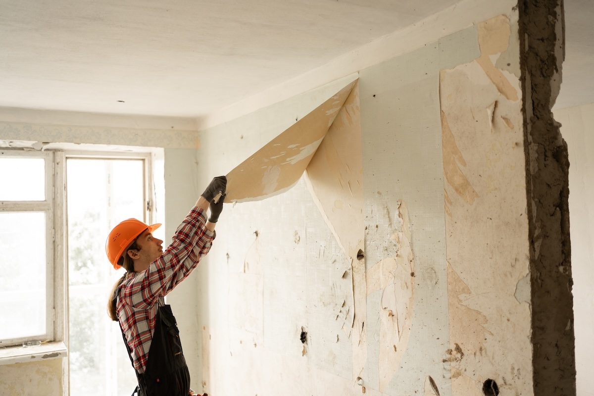 Young handyman removing wallpaper during home renovation