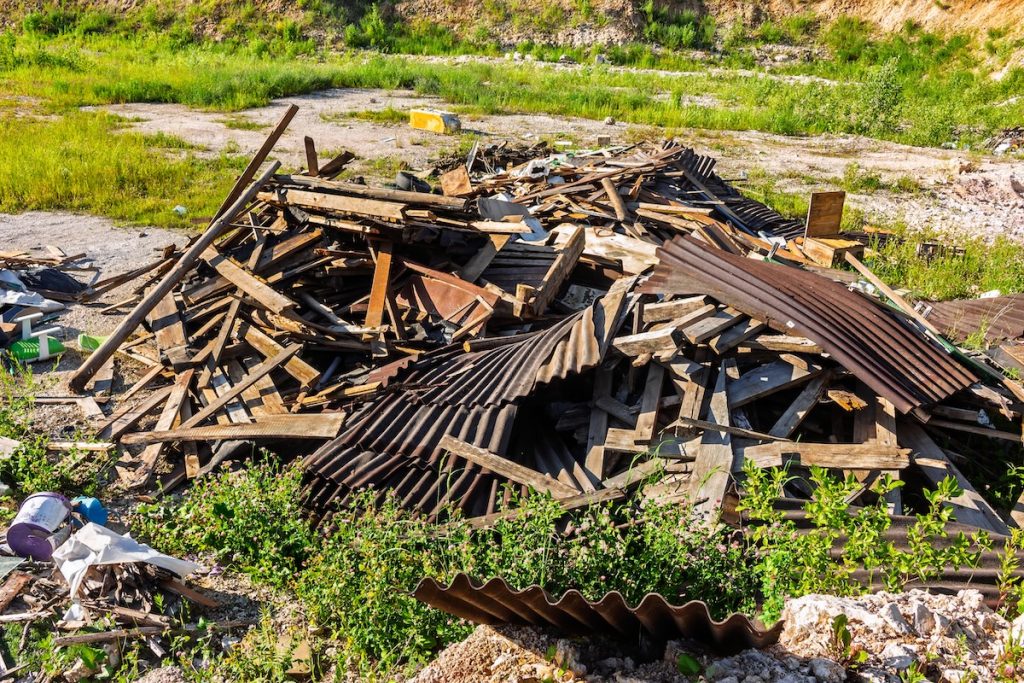 Heap of wooden planks and discarded corrugated slate sheets forming a messy pile of construction waste in a rural countryside landscape